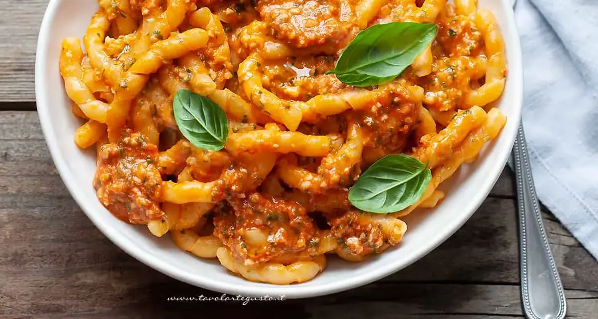 Un piatto invitante di busiate alla trapanese, condite con un sugo rosso e guarnite con foglie di basilico fresco.
