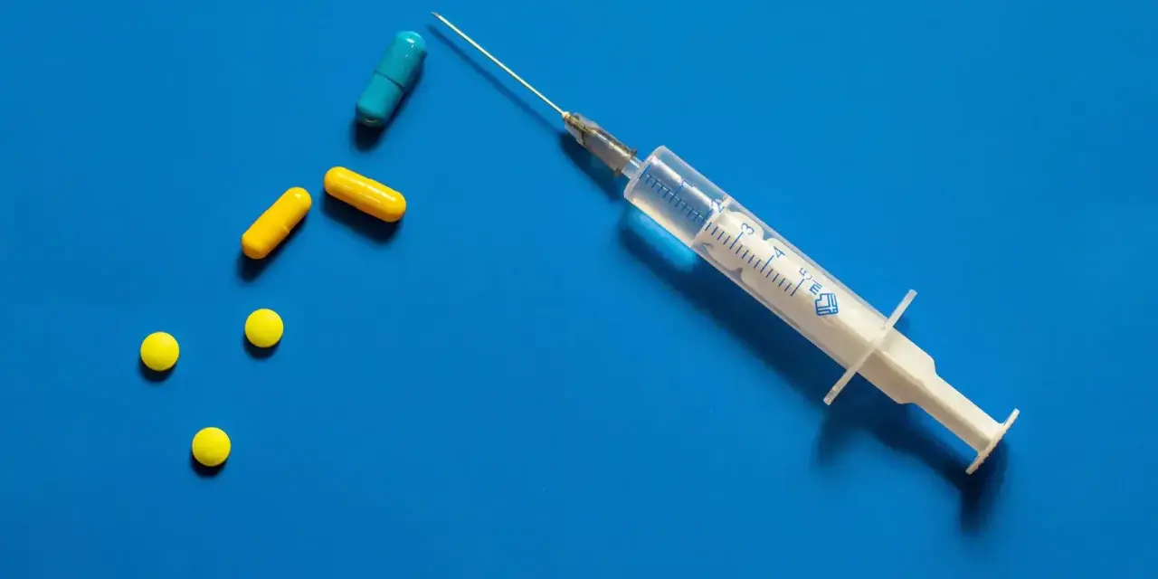 Strzykawka z igłą i kilka tabletek, w tym kapsułki. Może to być przygotowanie do zastrzyku hormonalnego.
