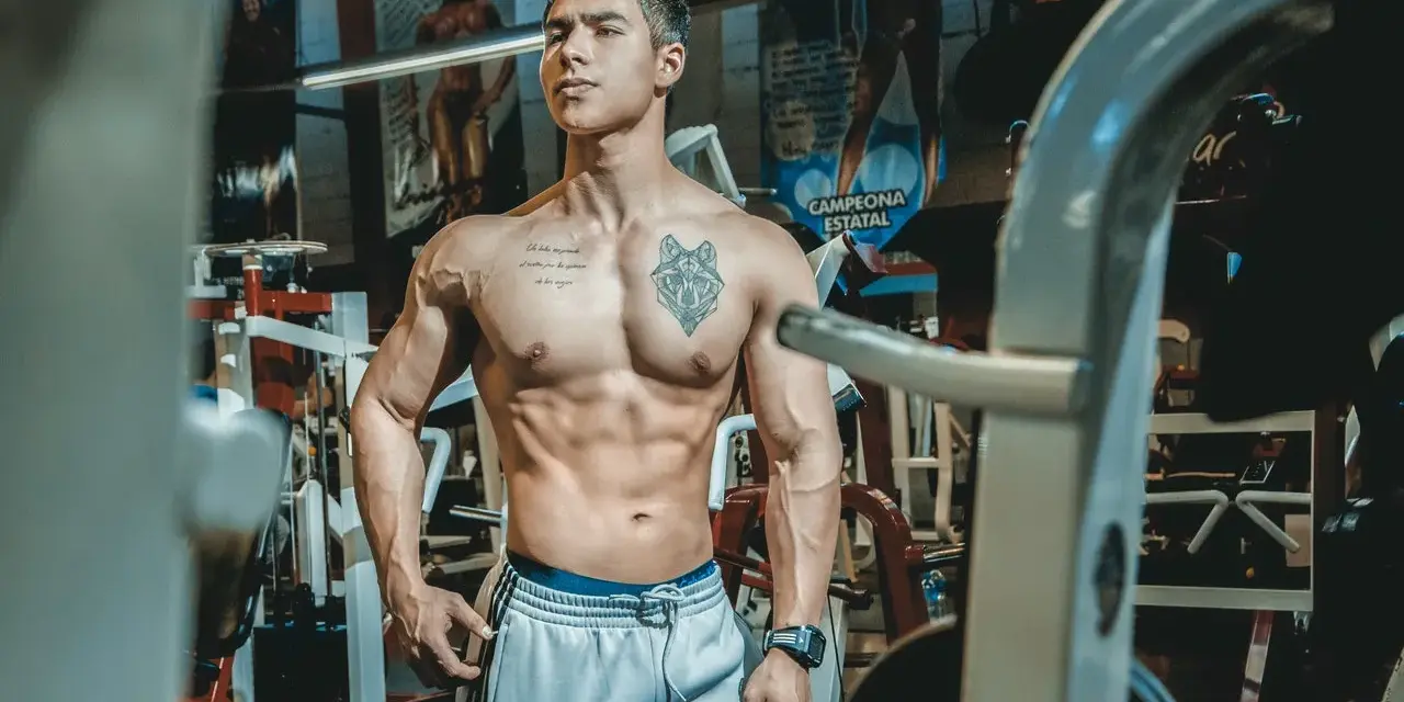 Muskulös man med tatueringar i gym. Han har en imponerande fysik, ett resultat av hårt arbete och att **deffa mat**.