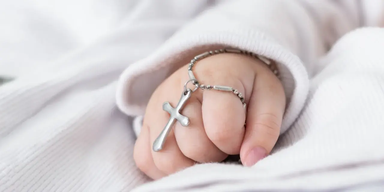 Dziecięca dłoń z krzyżykiem na bransoletce, symbol błogosławieństwa podczas chrzcin dziecka.