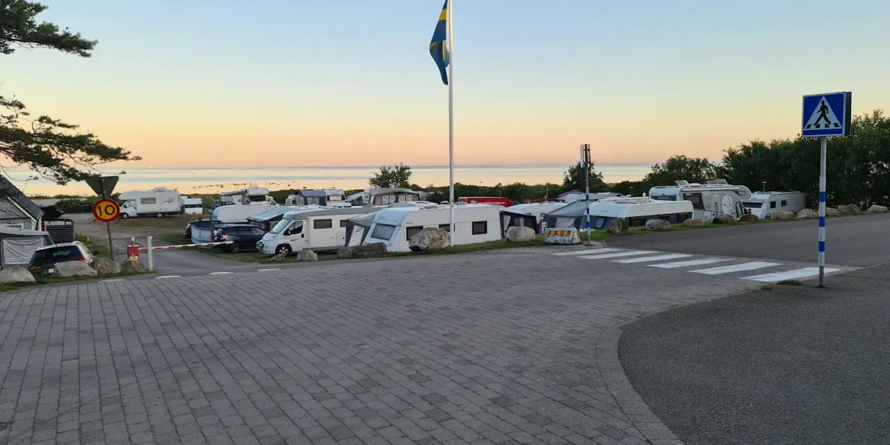 Solnedgång över Lerbergets camping med husbilar och husvagnar uppställda. En svensk flagga vajar i vinden.