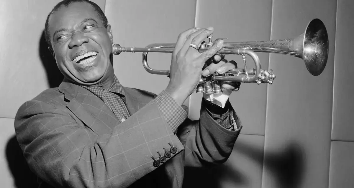 Louis Armstrong, znany jako "Satchmo", gra na trąbce z charakterystycznym uśmiechem.