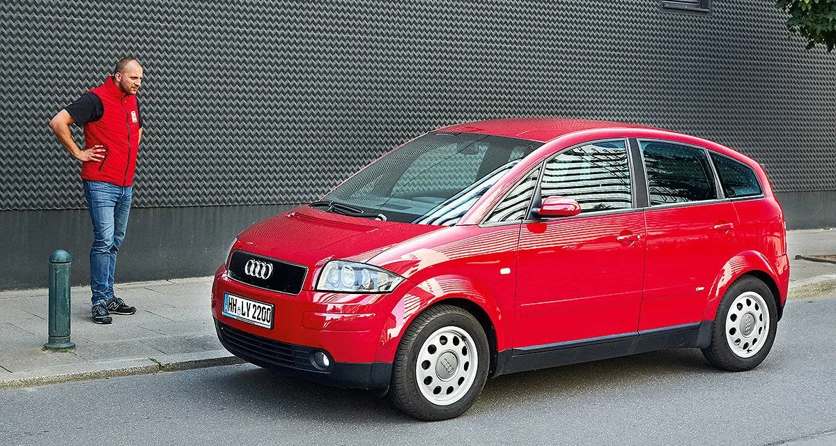 Mann steht neben rotem Audi A2, der für seine audi a2 schwachstellen bekannt ist.