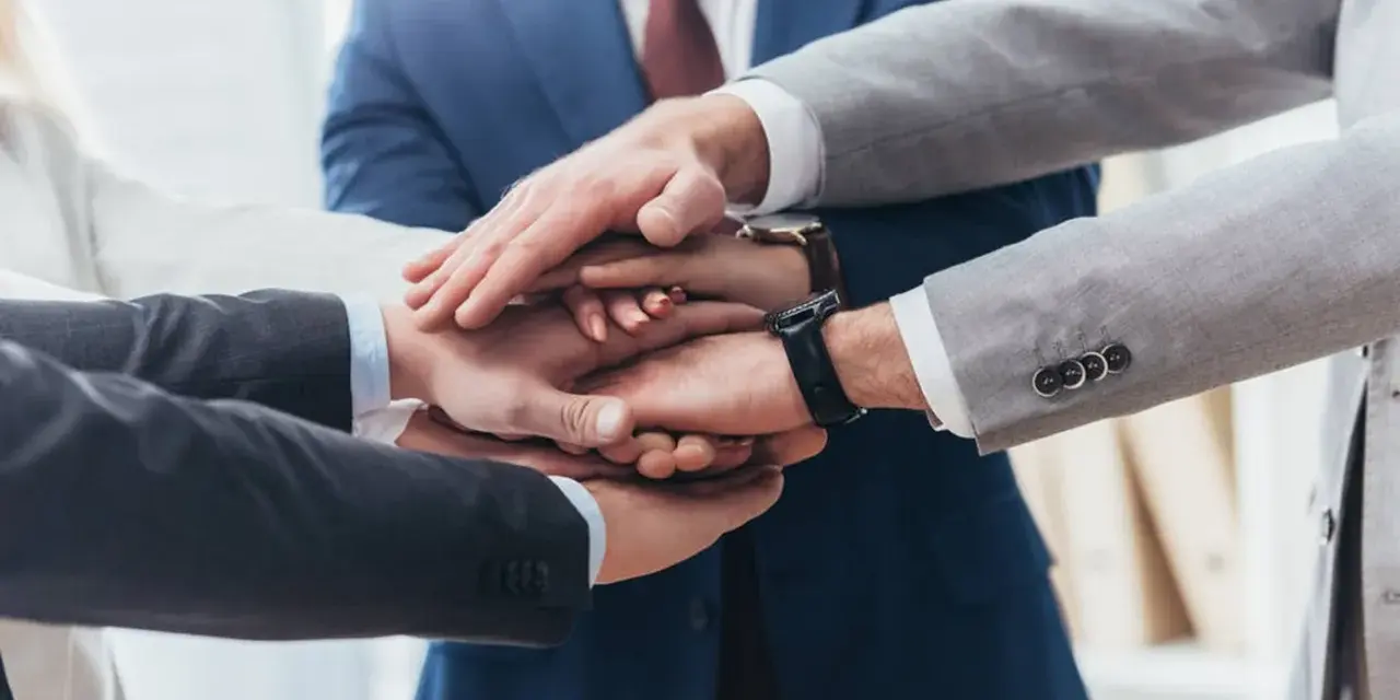 Zespół składa dłonie, symbolizując jedność i siłę. To jak prokura samoistna – wspólne działanie dla dobra firmy.