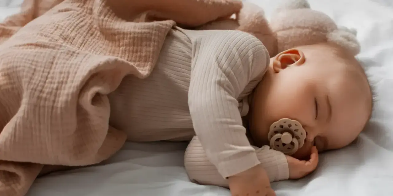 Malutkie dziecko śpi na brzuchu, otulone miękkim kocykiem. Smoczek w buzi zapewnia mu spokojny sen.