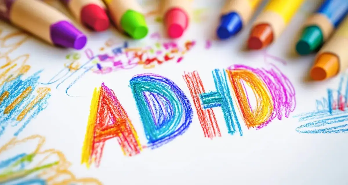 Kolorowe kredki otaczają napis "ADHD" narysowany na białej kartce. Dziecko, które nie jest neurotypowe, wyraża siebie przez sztukę.