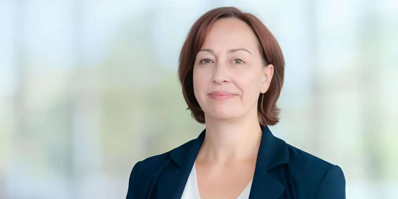 Agata Witkowska, aktorka, w granatowej marynarce i białej bluzce, uśmiecha się lekko.