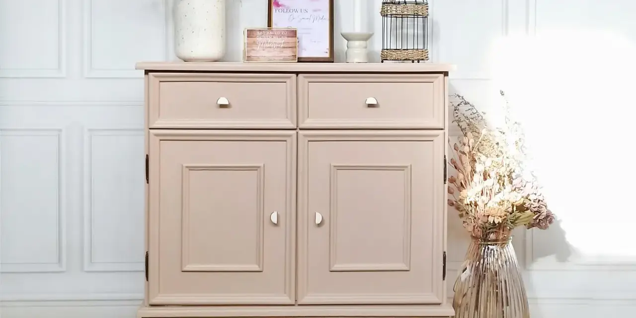 Meuble ancien repeint en rose poudré, avec deux tiroirs et deux portes. Décoré de fleurs séchées et d'une cage à oiseaux.