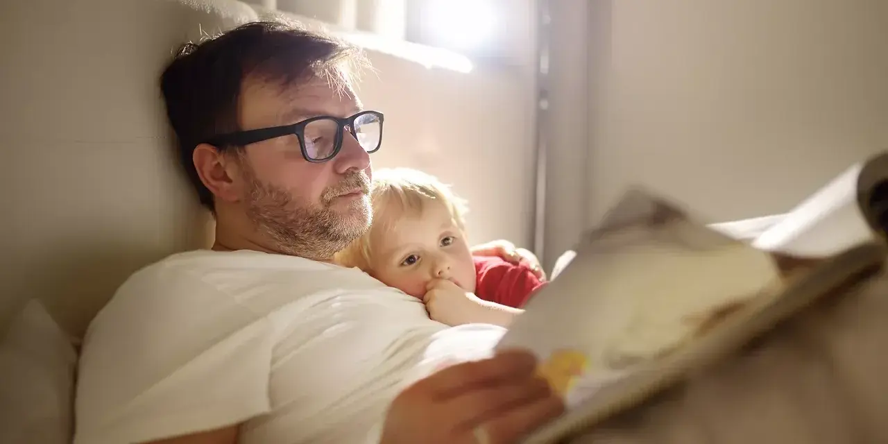 Vater im Elternzeit, 1 Monat alt, liest seinem Kind im Bett eine Geschichte vor.
