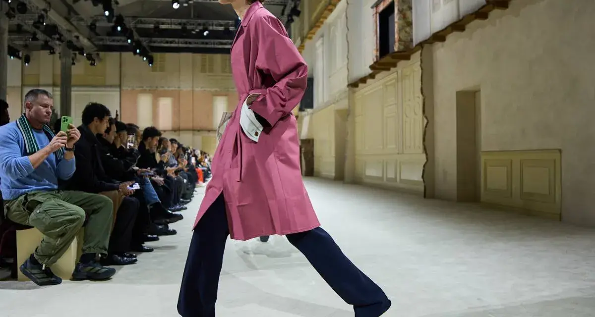 Modello sfila con trench rosa e pantaloni blu, un esempio di moderno stile uomo.