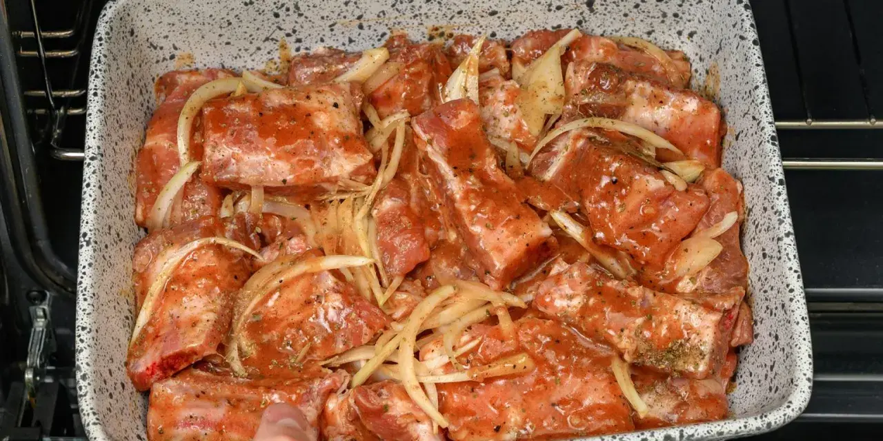 Babcine żeberka w sosie własnym, gotowe do pieczenia. Mięso w sosie z cebulą, przyprawione ziołami, w naczyniu żaroodpornym.