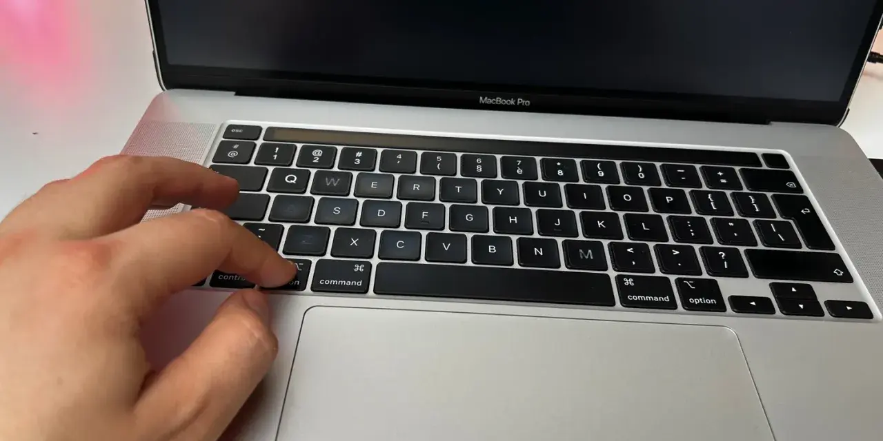 Dłoń naciska klawisz "command" na klawiaturze MacBooka, przygotowując się do instalacji drukarki.