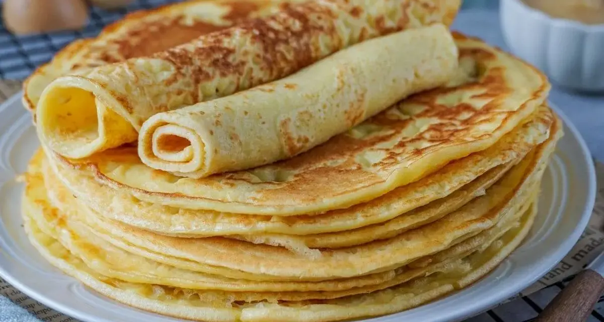 Ein Stapel goldbrauner Eierkuchen, zwei davon gerollt, perfekt für ein einfaches Eierkuchen Rezept.