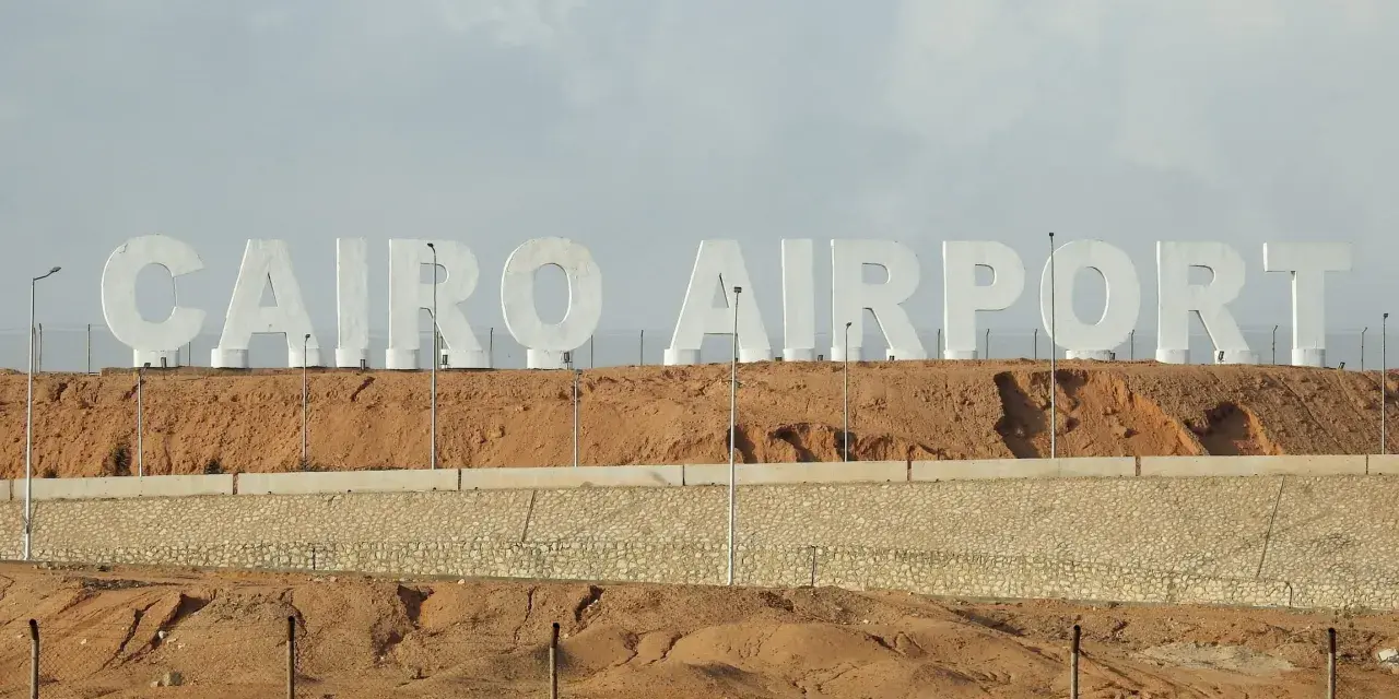 Ogromne białe litery "CAIRO AIRPORT" na tle pustynnego krajobrazu. Jedno z lotnisk w Egipcie.