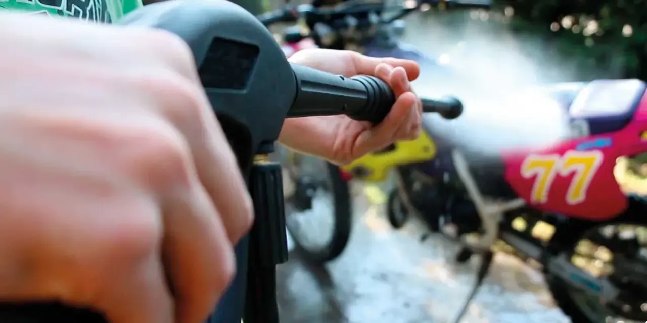 Mani che impugnano un'idropulitrice per pulire una moto da cross. Un modo efficace per capire come lucidare la moto.