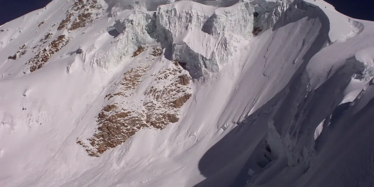 Schneebedeckte Gipfel des Huayna Potosí, mit steilen Eiswänden und felsigen Hängen unter einem tiefblauen Himmel.