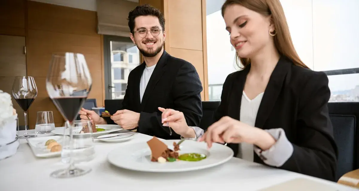 Elegancki strój na kolację do restauracji. Para w czarnych marynarkach delektuje się wykwintnym deserem przy kieliszkach czerwonego wina.