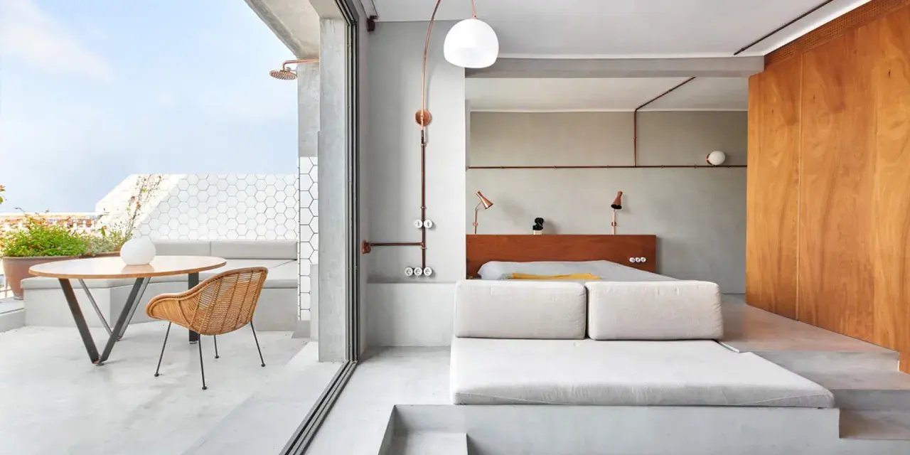 Habitación con diseño industrial, cama baja, sofá de lino y terraza con ducha exterior.