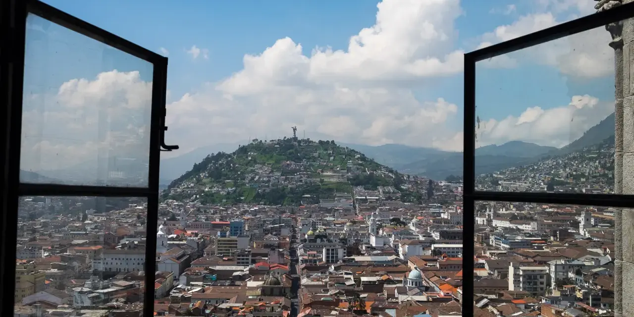 Widok na miasto z otwartego okna, z wzgórzem i pomnikiem w tle. To piękna panorama stolicy Ekwadoru, ze stolicą w Quito.