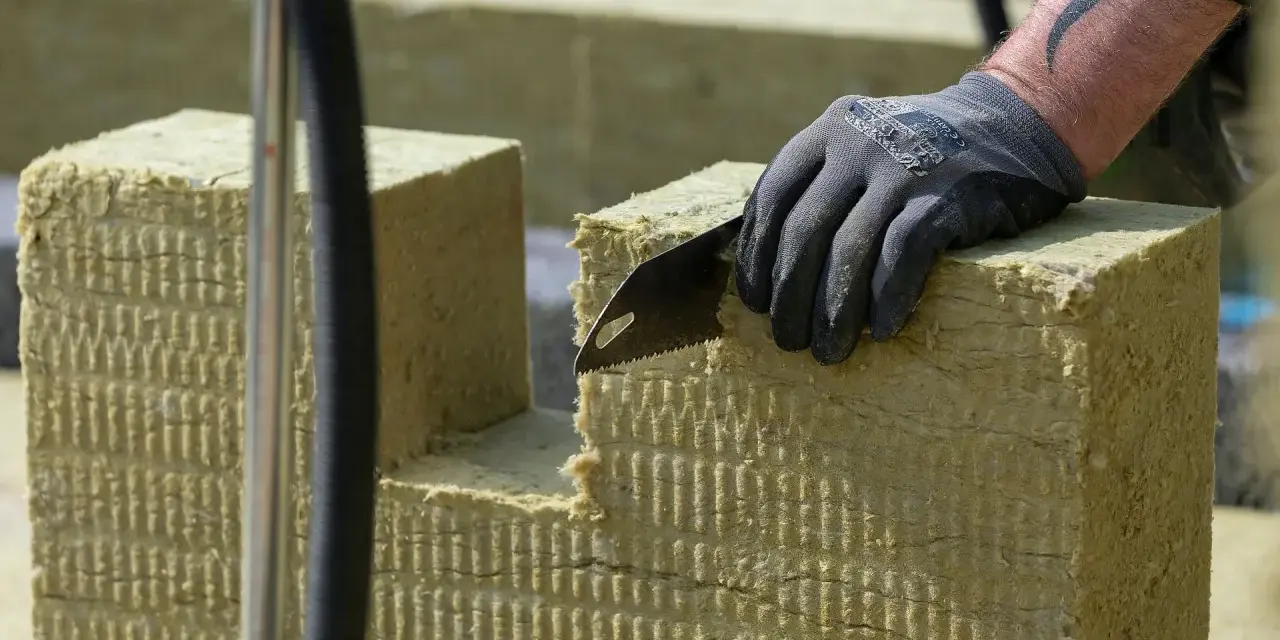Ręka w rękawicy tnie piłą wełnę skalną 10. Materiał izolacyjny jest przygotowywany do montażu.