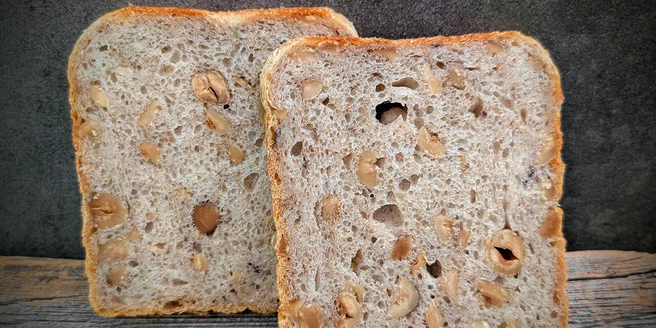 Zwei Scheiben salzarmes Brot mit Nüssen liegen auf Holz.