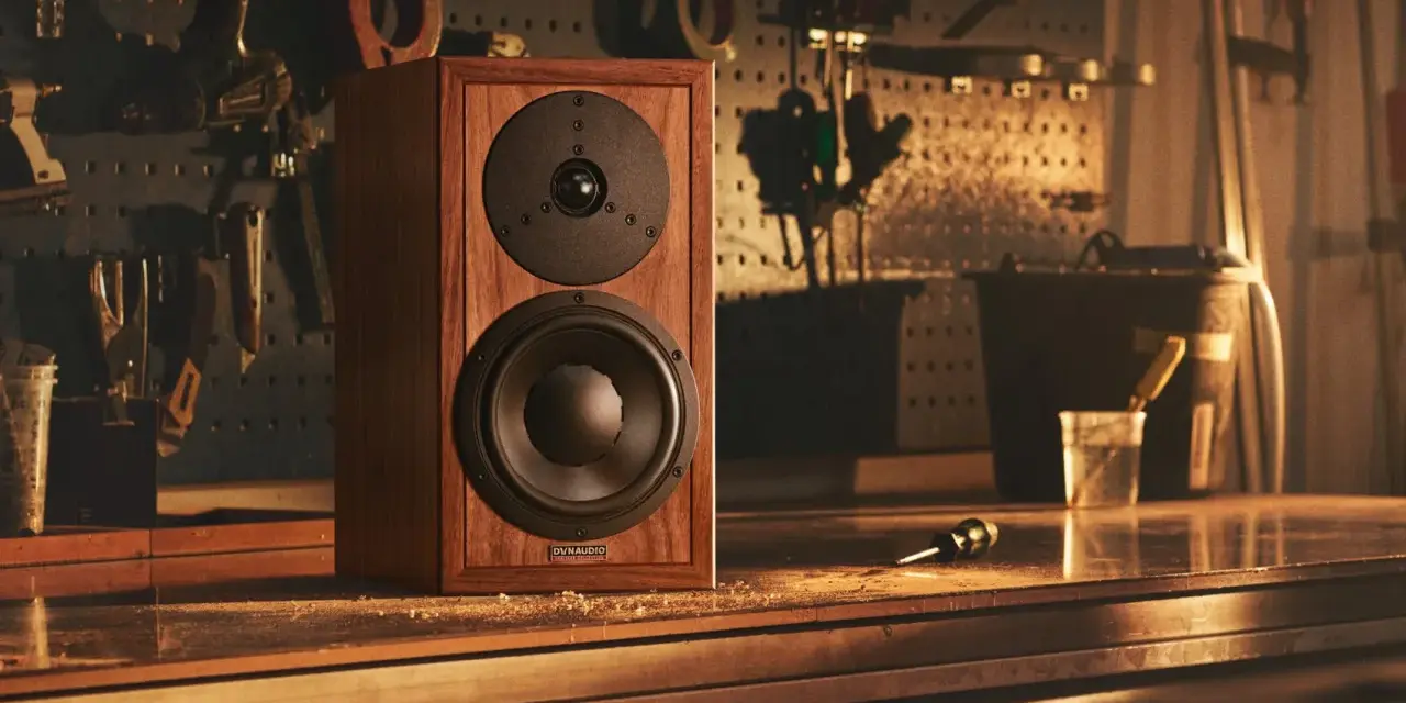 Głośnik Dynaudio Special 25 w drewnianej obudowie, stojący na stole w warsztacie, otoczony narzędziami.