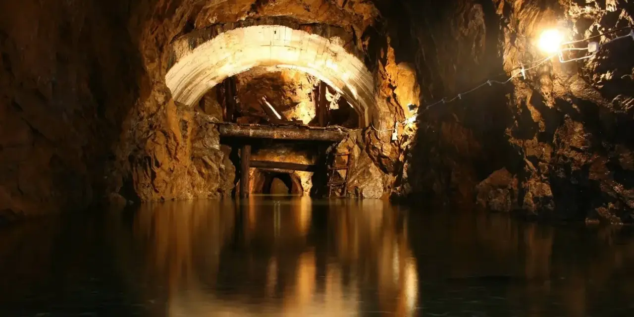 Podziemny kompleks włodarz, zalany wodą tunel kopalni z łukowym stropem i drewnianymi podporami.