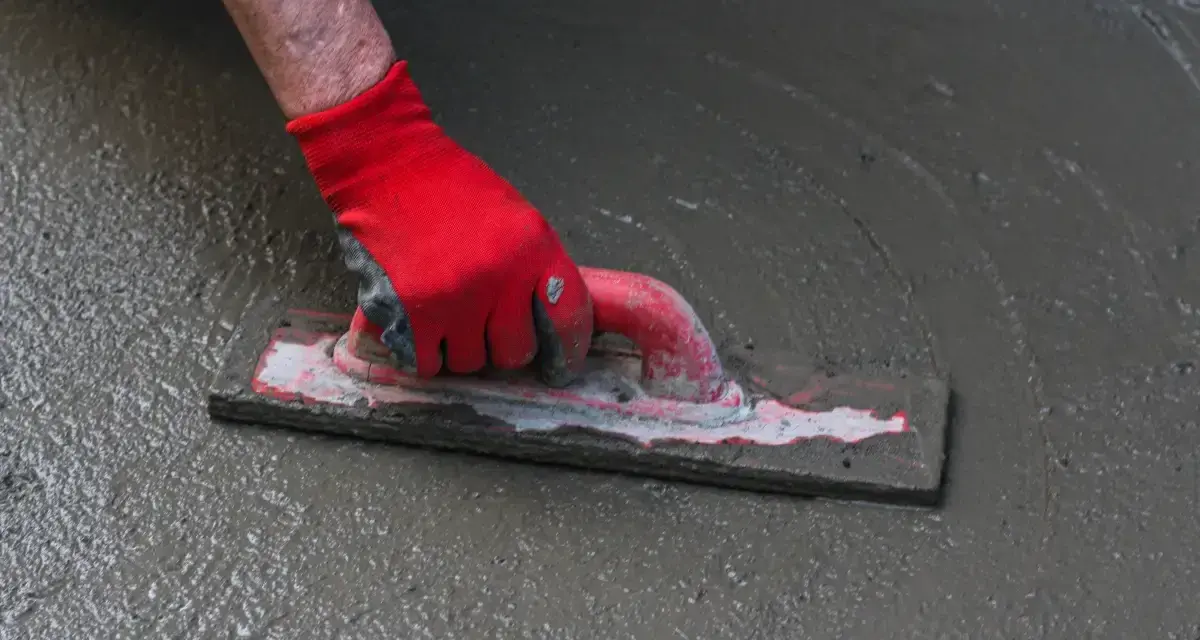 Ręka w czerwonej rękawicy wygładza świeżą wylewkę do garażu za pomocą kielni.