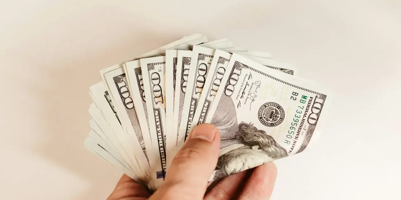 Dłoń trzyma plik banknotów 100 dolarowych. To może być kwota na spłatę PCC od pożyczki.