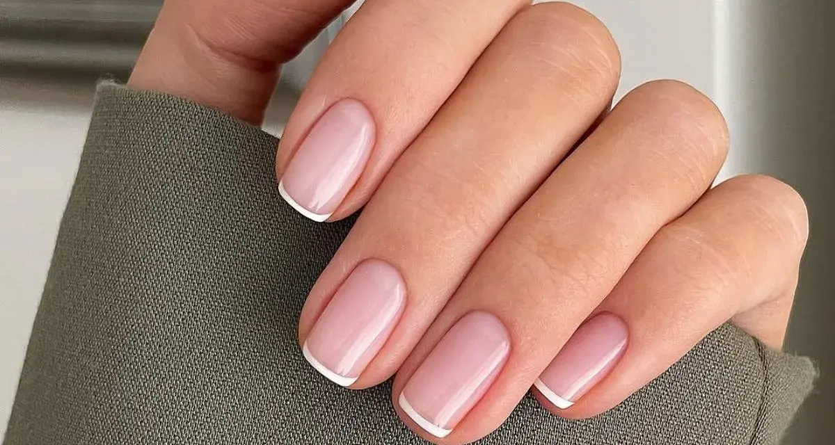 Dłoń z idealnymi, różowymi paznokciami i białymi końcówkami – klasyczne french nails.