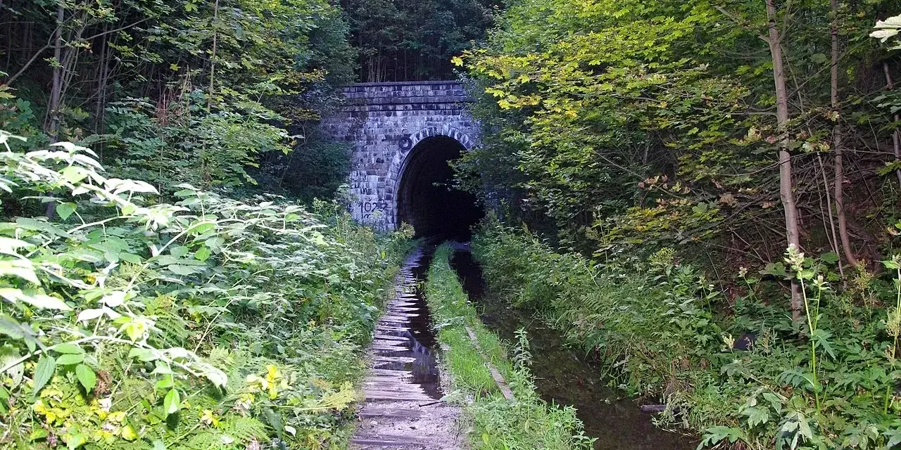 Kamienna, kameralna brama do mrocznego tunelu kolejowego w Kowarach, otoczona bujną zielenią.