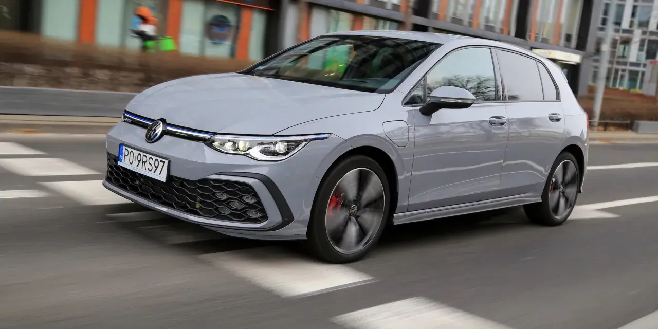 Szary Volkswagen Golf GTE porusza się po miejskiej drodze, z rozmytym tłem budynków i przechodniów.
