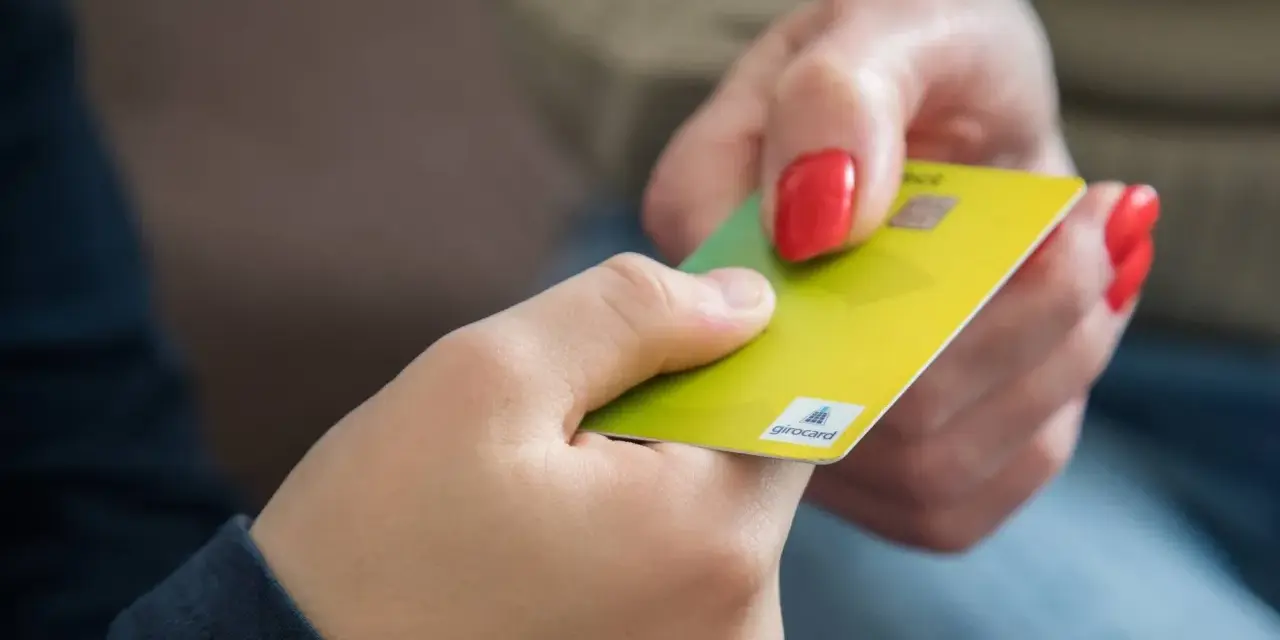 Eine Hand gibt einer anderen eine gelbe Girocard. Dies könnte die erste kinder debitkarte sein, die ein Kind erhält.