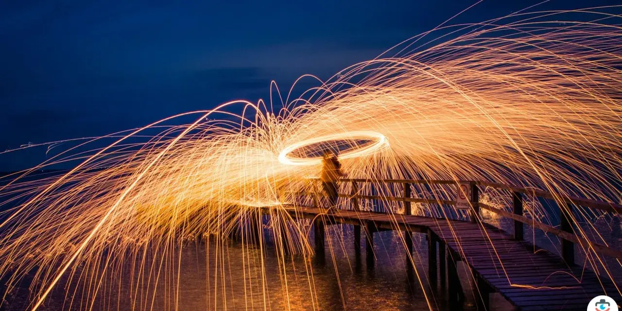Une personne sur un pont crée une **light painting photo** spectaculaire avec des traînées de feu dans le ciel nocturne.