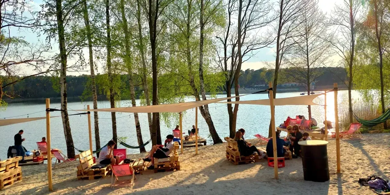 Relaks na plaży nad jeziorem, idealne miejsce na camping Polska. Ludzie odpoczywają na leżakach i paletach pod namiotami.