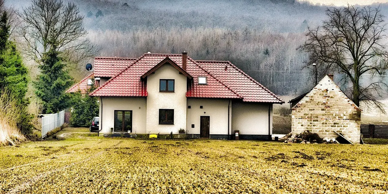 Dom z czerwonym dachem i polem przed nim. Rodzinna historia o przepisaniu domu na jedno dziecko bez zgody drugiego.