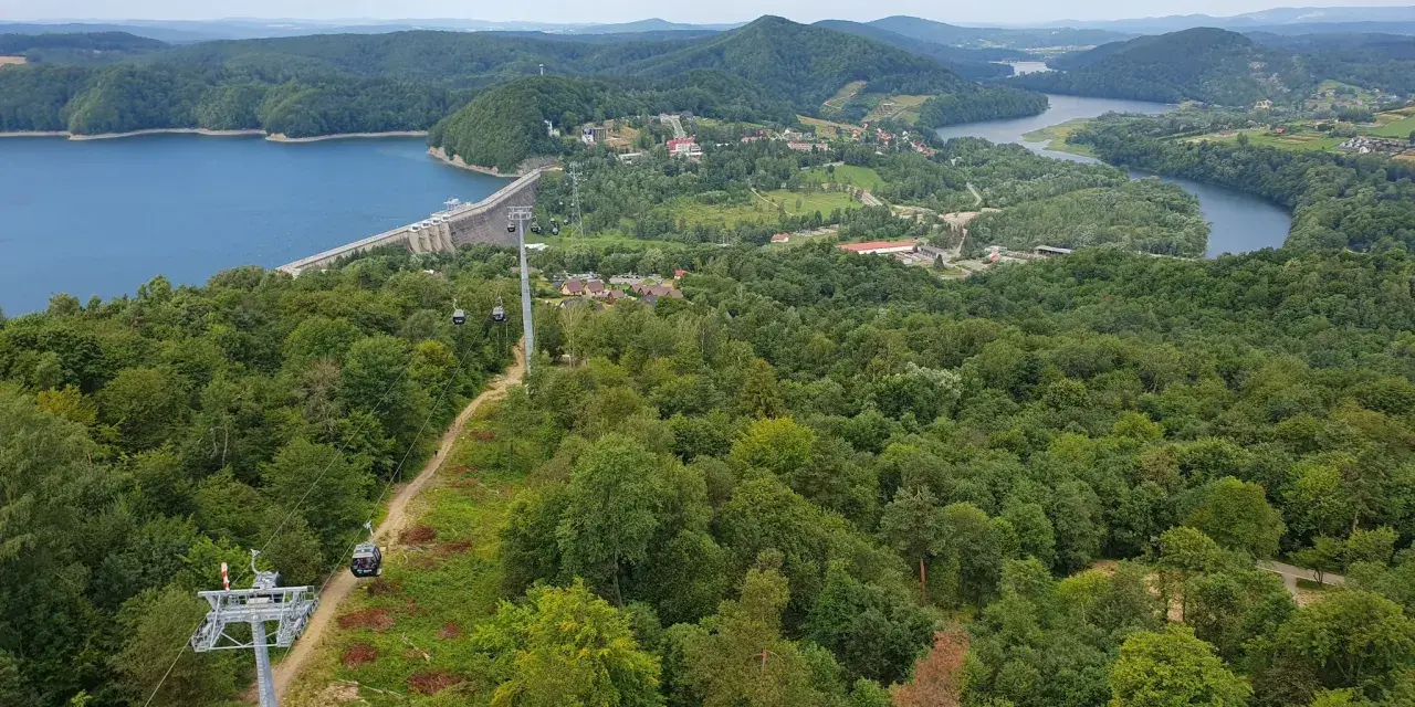 Widok na zielone wzgórza nad Soliną, z widoczną zaporą, jeziorem i kolejką gondolową. Trasa widokowa zachwyca.