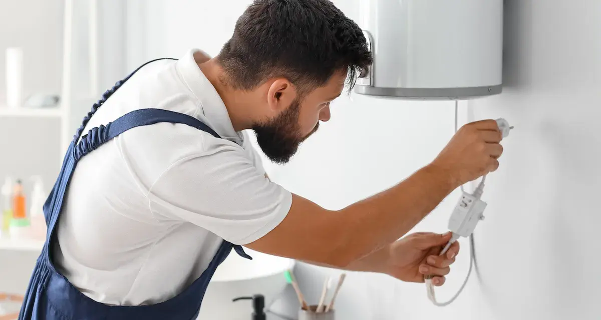 Tecnico con tuta blu controlla la caldaia. La manutenzione caldaia a chi spetta? Al tecnico specializzato, per la sicurezza di tutti.