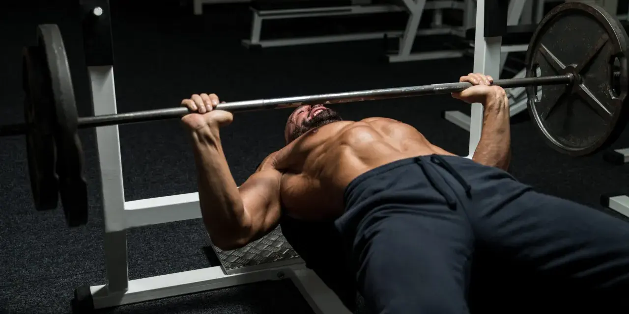Man med skägg och synliga muskler utför bänkpress som en del av sitt starting strength program.