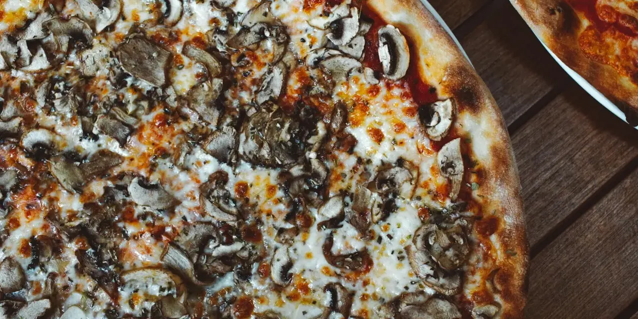Pyszna pizza wegetariańska z pieczarkami i ciągnącym się serem, idealna na wspólny wieczór.