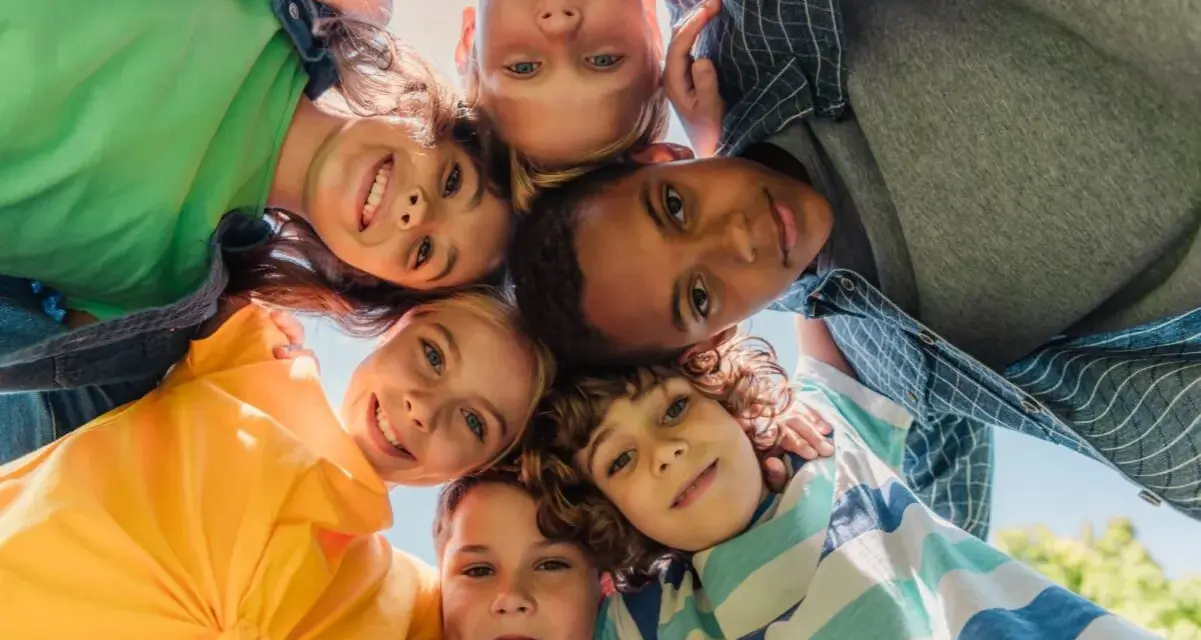 Un groupe d'enfants souriants forme un cercle, leurs visages se rejoignant au centre. Leurs regards joyeux et leurs expressions témoignent d'un bel encadrement d'enfants.