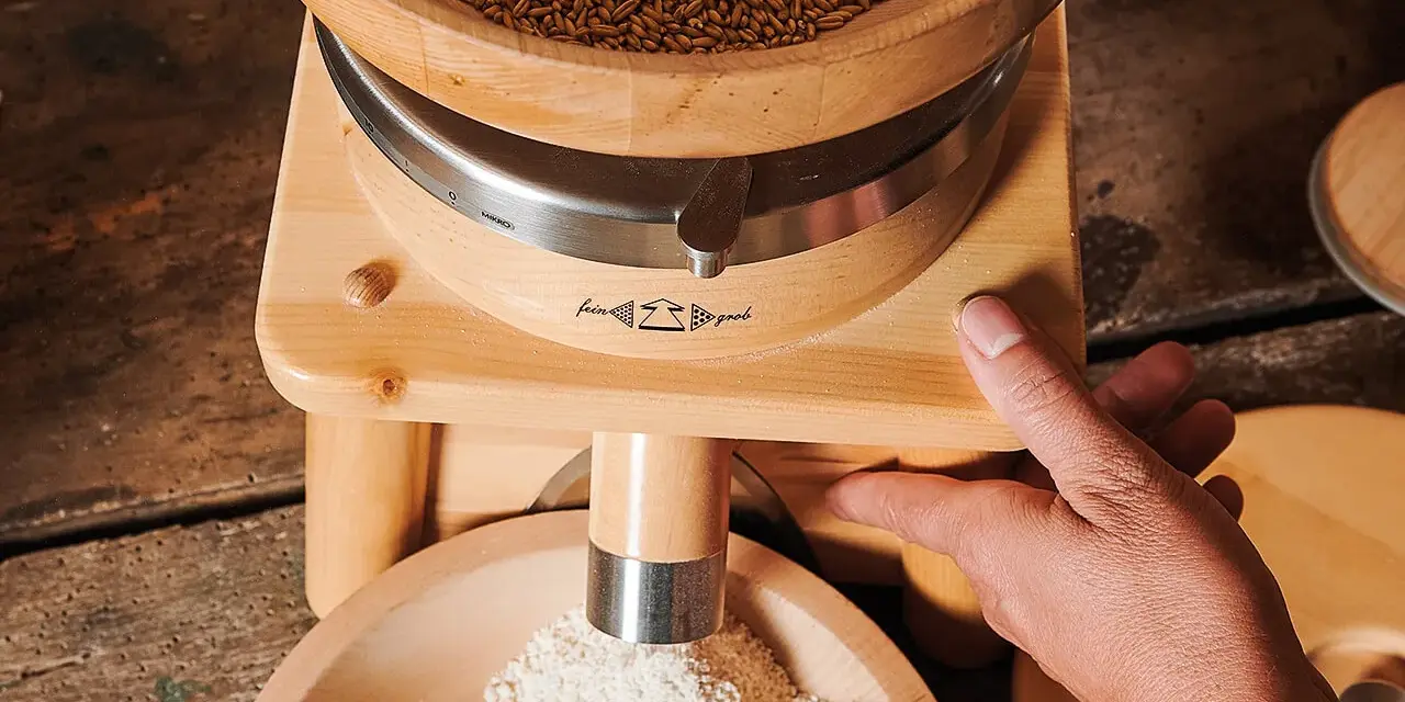 Holzgetreidemühle mit Getreide oben und frisch gemahlenem Mehl unten, Hand bedient die Mühle.