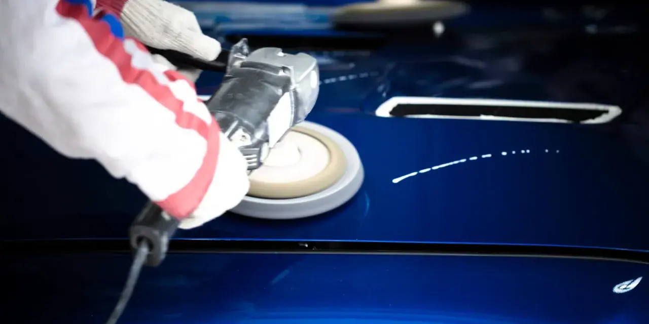 A gloved hand uses a buffer to polish a shiny blue car hood, demonstrating how to polish a car with a buffer for a flawless finish.