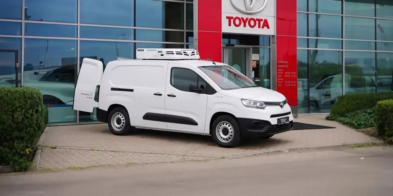 Biały, mały dostawczak z chłodnią na dachu stoi przed salonem Toyoty.