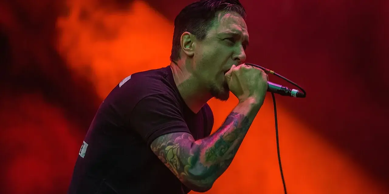 Chanteur au micro, le regard intense, comme s'il en avait marre de tout. Lumières rouges et orangées.