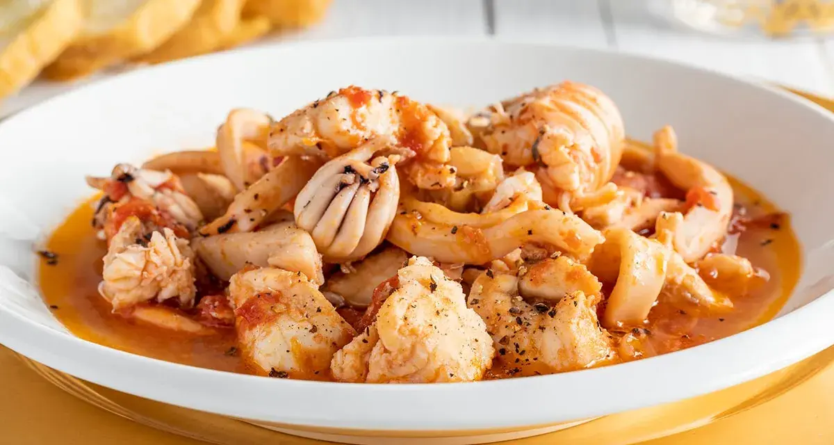 Un invitante piatto di zuppa di pesce, ricco di calamari, gamberi e pesce bianco, servito con crostini dorati.