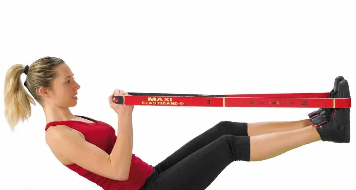 Femme faisant un exercice avec un élastique, jambes tendues et mains tenant la bande rouge.