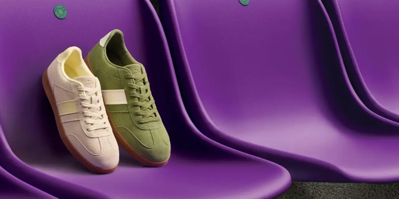 Due sneakers Clarks, una beige e una verde, sedute su sedili viola. Le Clarks calzano mezza misura in meno, perfette per un look casual.