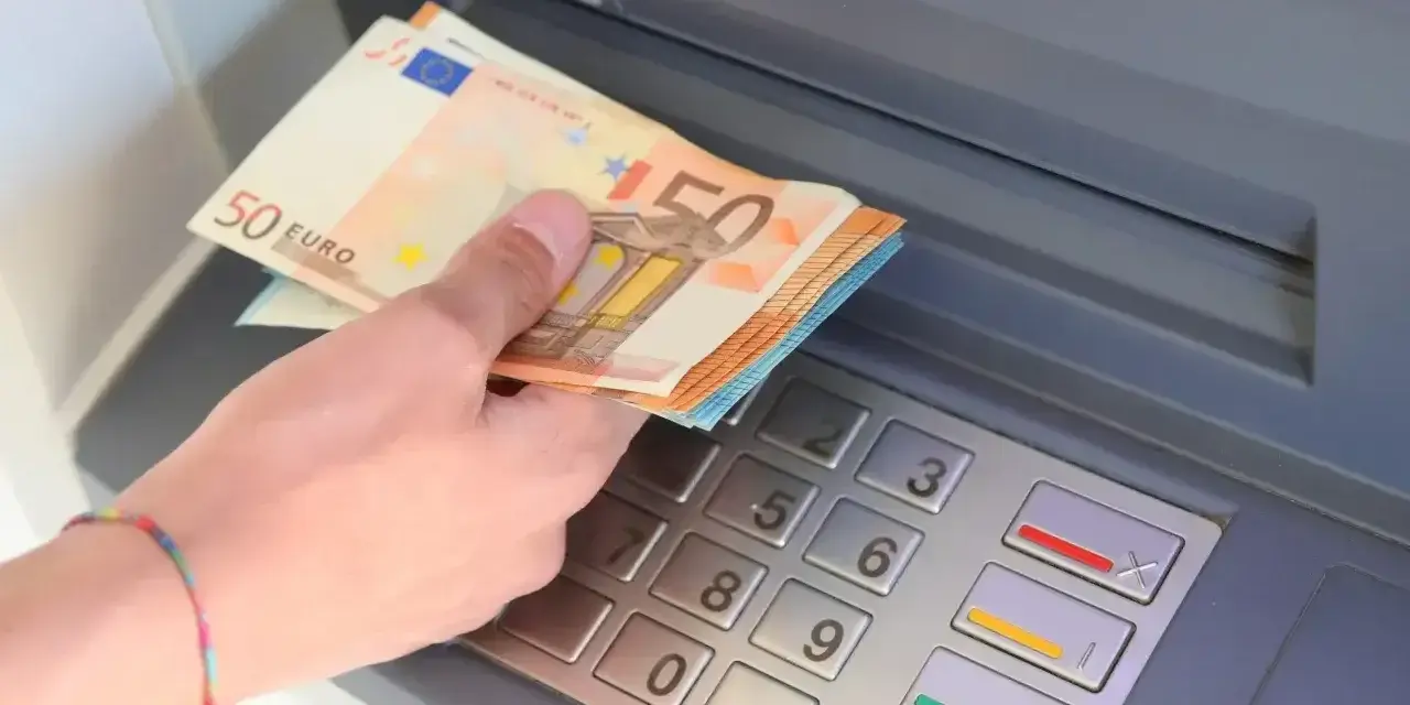 Dłoń trzyma banknoty 50 euro przy bankomacie. W Hiszpanii, jak w całej strefie euro, obowiązuje euro.