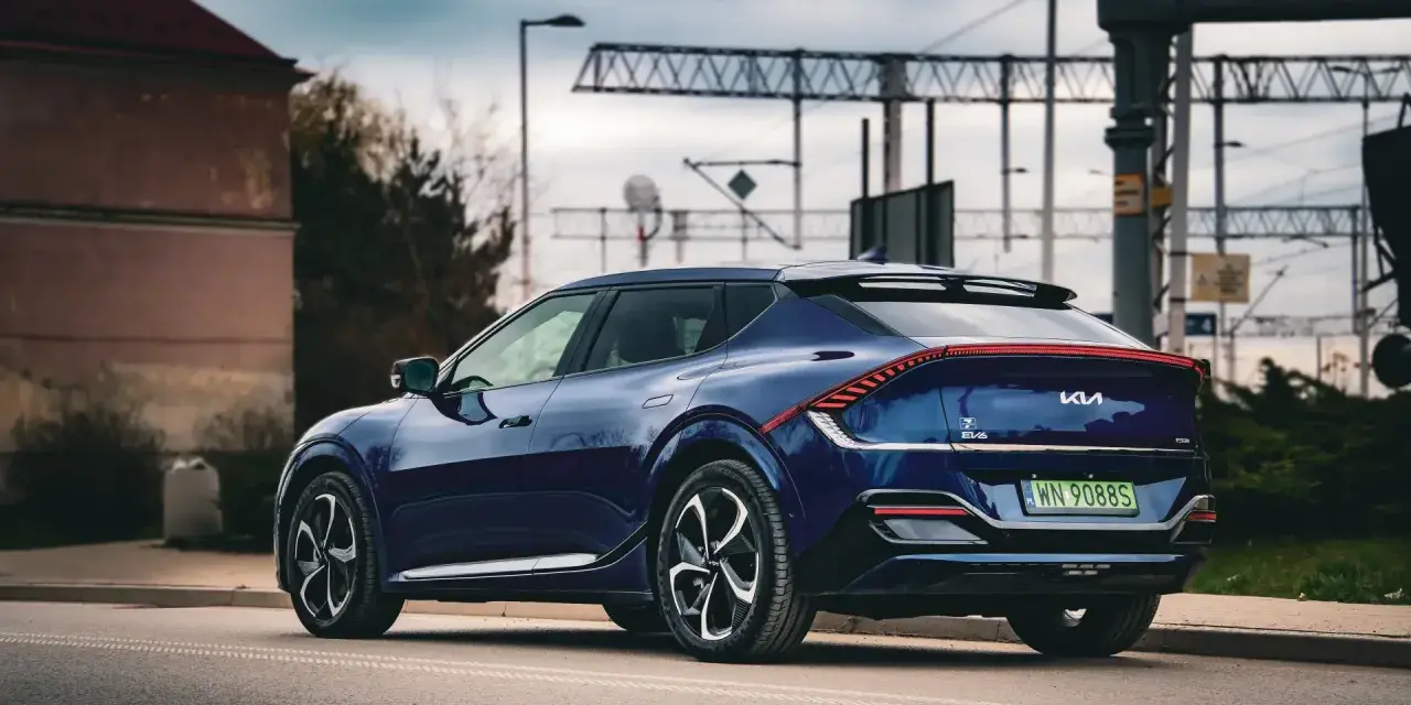 Granatowe Kia EV6 GT z charakterystycznym pasem świateł z tyłu, zaparkowane przy drodze z widoczną infrastrukturą kolejową.